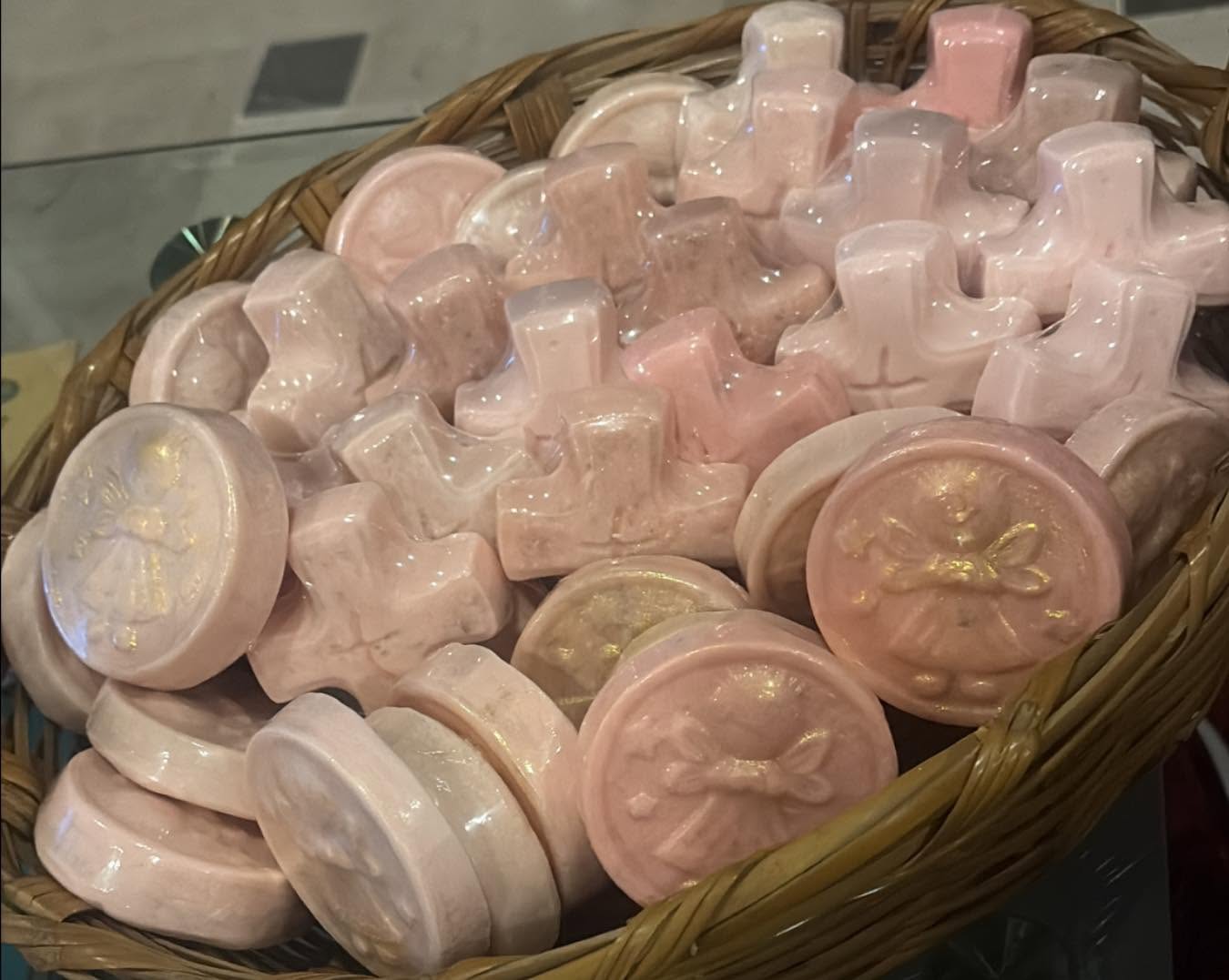Jabones artesanales rosados con formas de cruz y medallón, en una canasta